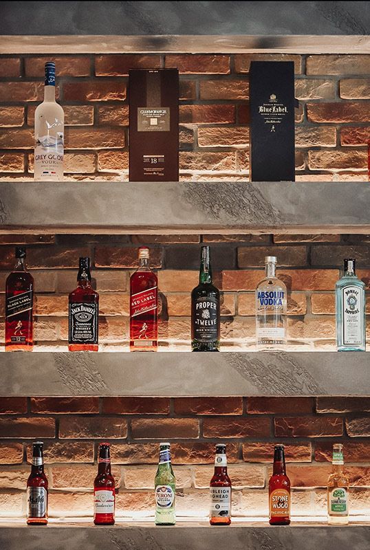 A Shelf Filled With Bottles of Liquor Against a Brick Wall — Barber Bros & Co - Southport in Southport, QLD