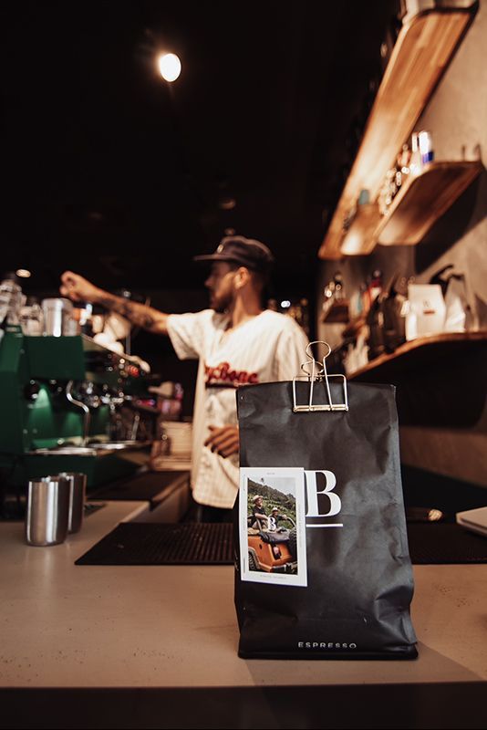 A Man is Standing Behind a Counter With a Bag of Coffee on It — Barber Bros & Co - Southport in Southport, QLD
