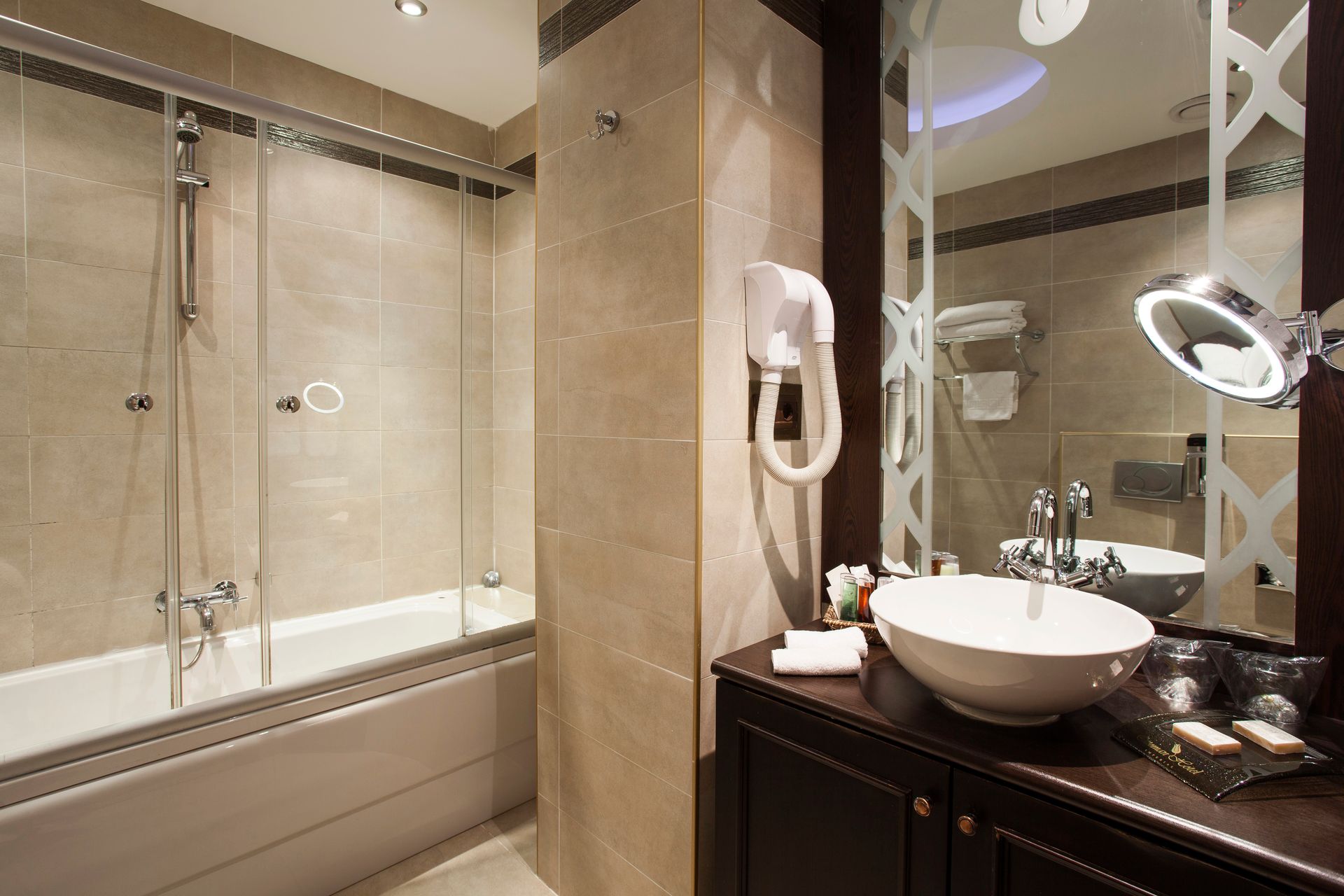 Ottoman Hotel Imperial| Bathroom with a bathtub and shower, vanity with sink, mirror, and hairdryer. Neutral tones.