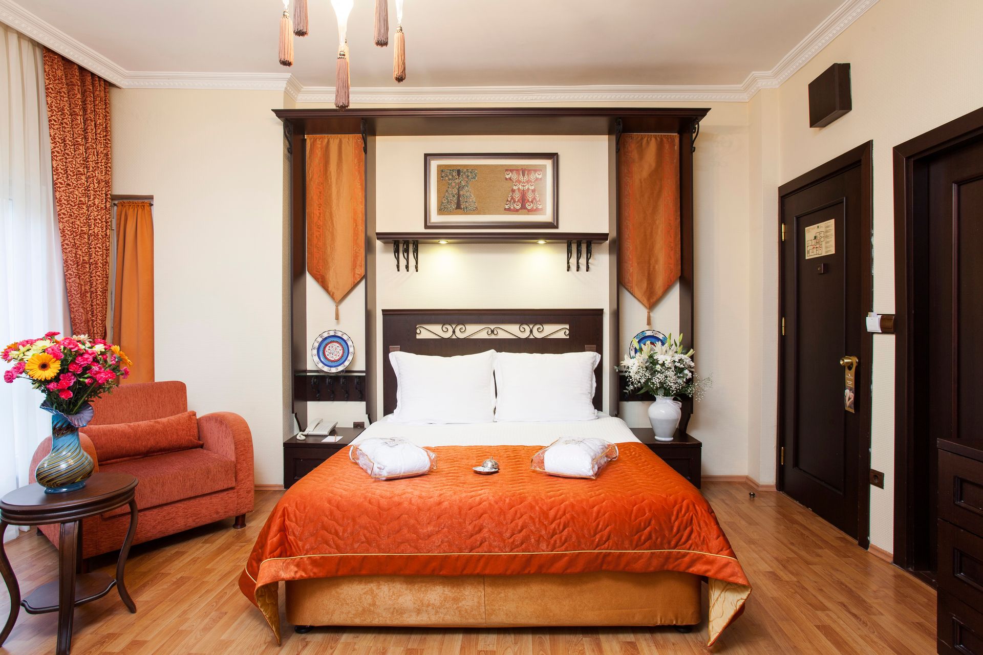 Ottoman Hotel Imperial| Hotel room with double bed, orange bedding, wooden furniture, flowers, and two closed brown doors.
