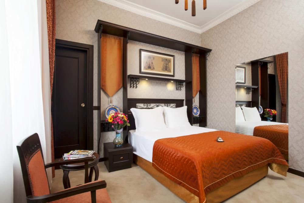 Ottoman Hotel Imperial| Hotel room with a bed, nightstand, chair, mirror, and a dark wood headboard with decorative panels.