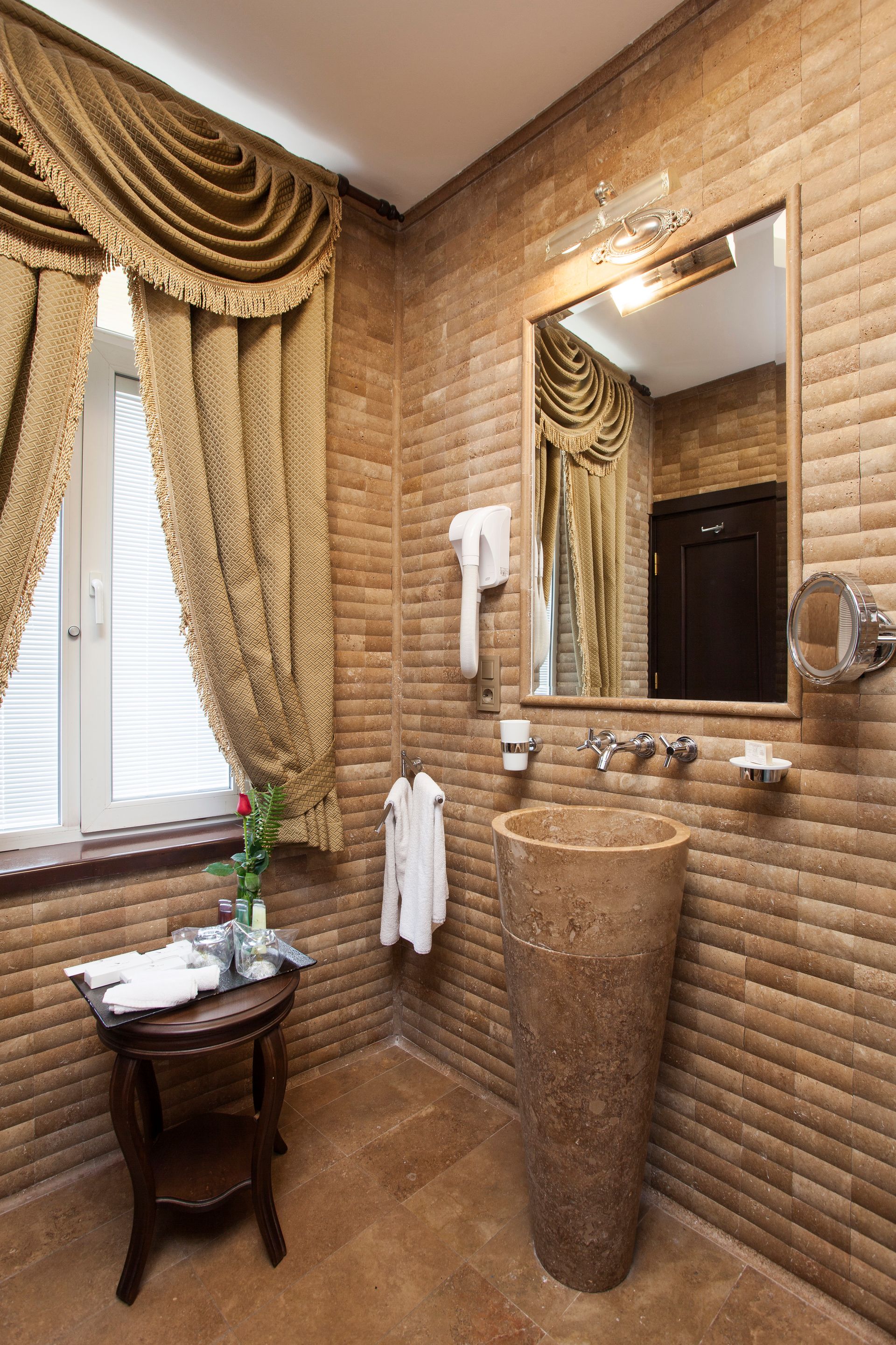 Bathroom with brown textured walls, tall pedestal sink, window with gold curtains, and a mirror.