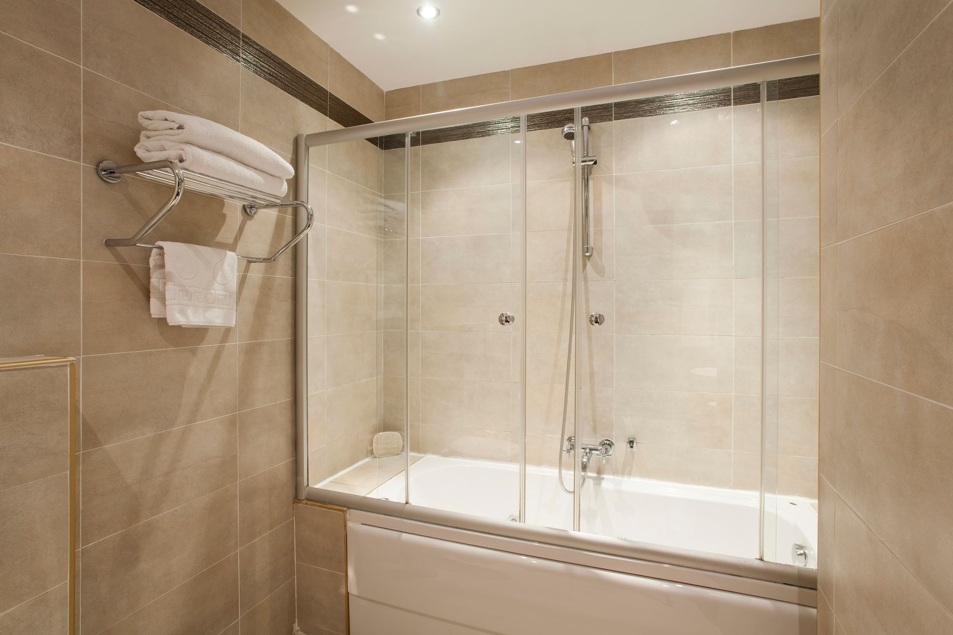 Ottoman Hotel Imperial|Bathroom with a white bathtub, glass shower screen, and towel rack with folded white towels.
