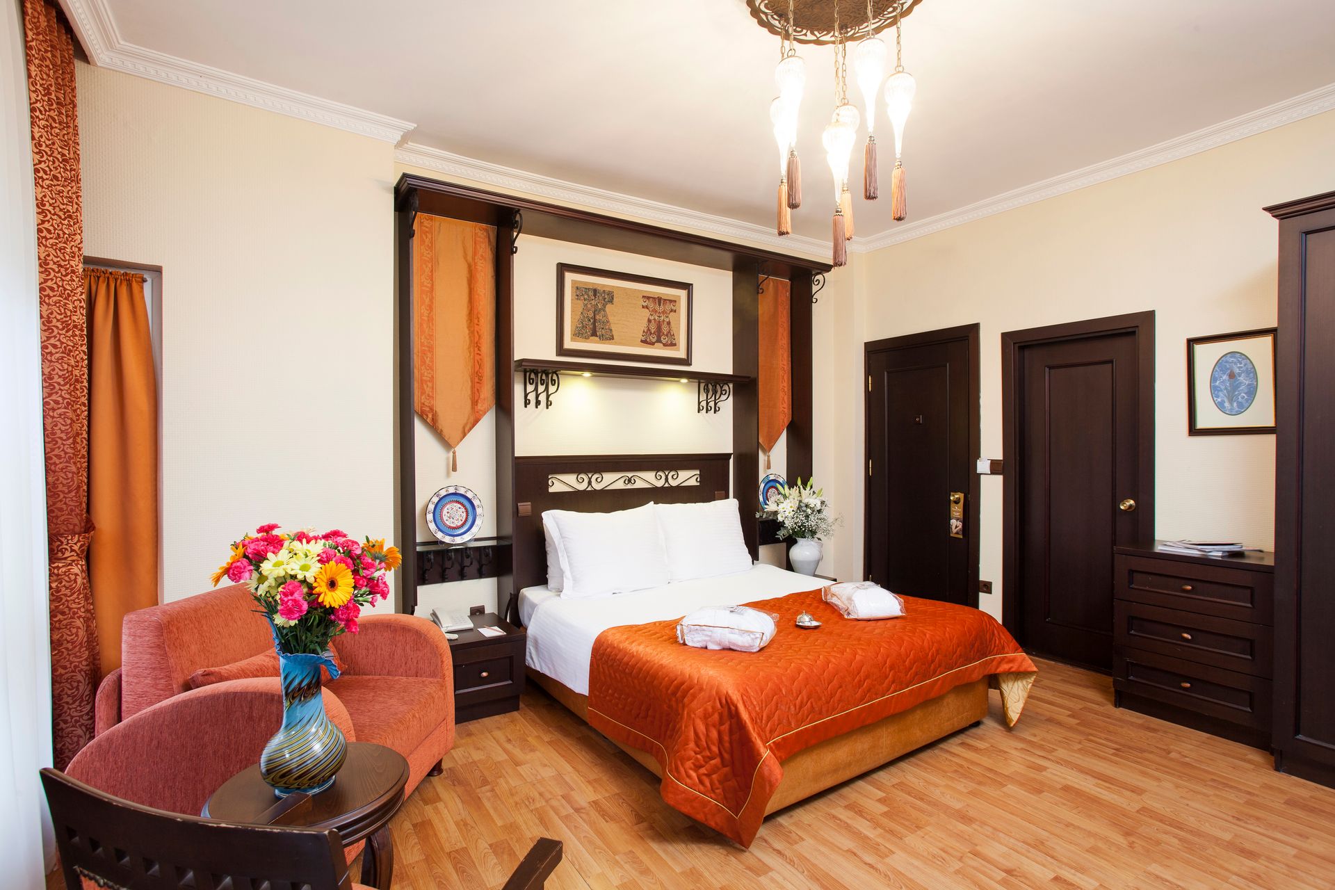 Ottoman Hotel Imperial| Hotel bedroom with orange accents, wooden furniture, and a bed with white linens and a folded towel.