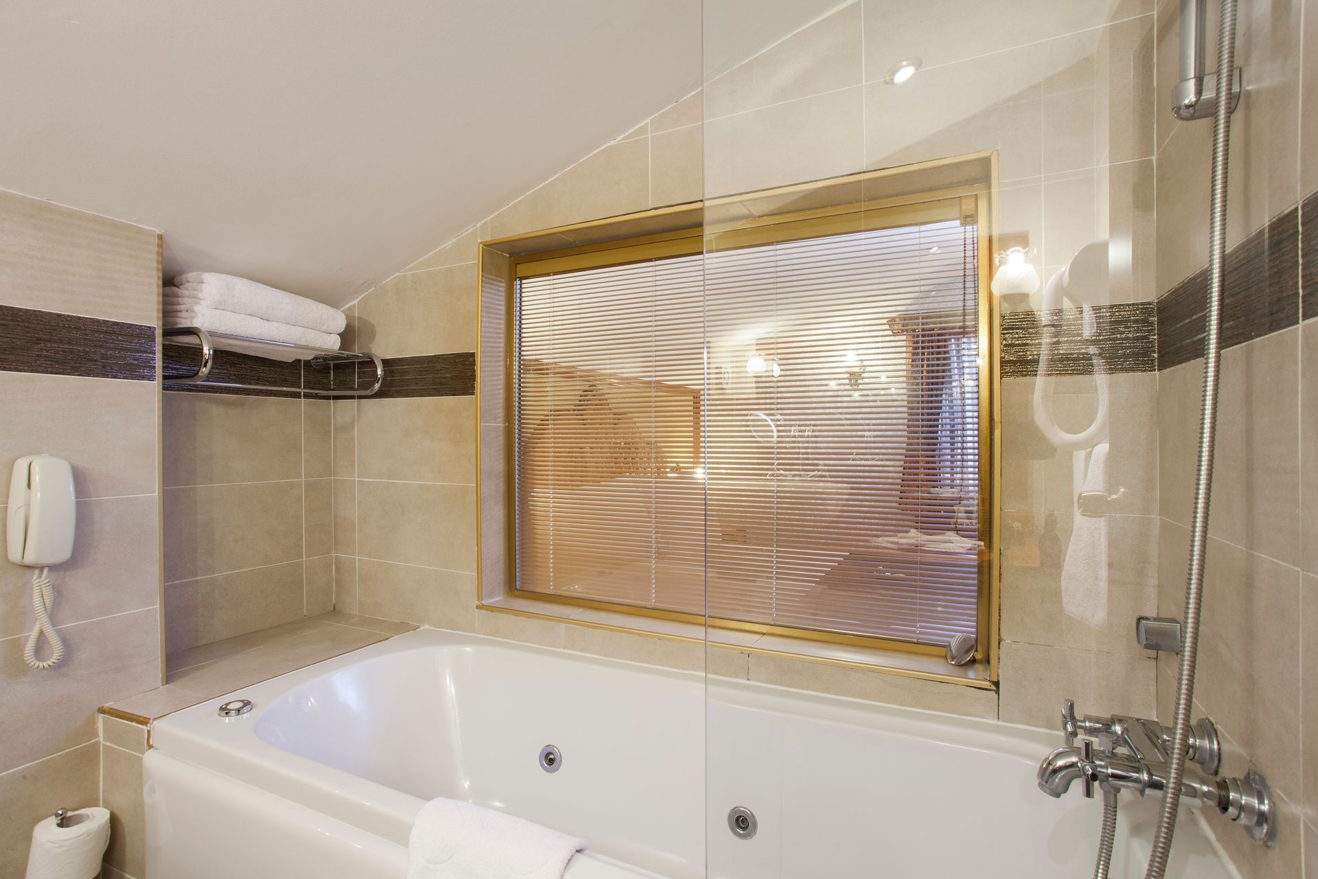 Bathroom with a white jacuzzi tub, frosted window, showerhead, and tiled walls.