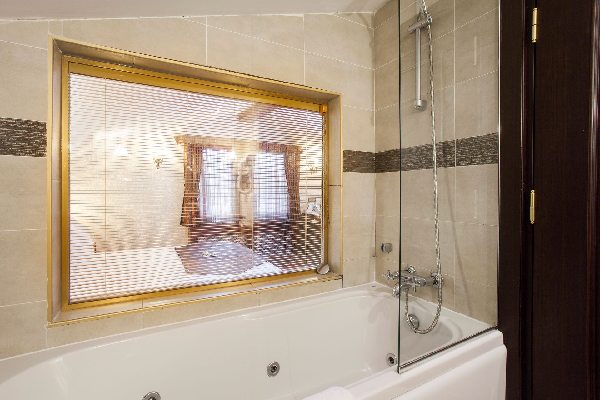 Bathroom with jacuzzi tub, glass shower, and window with patterned glass and golden frame.