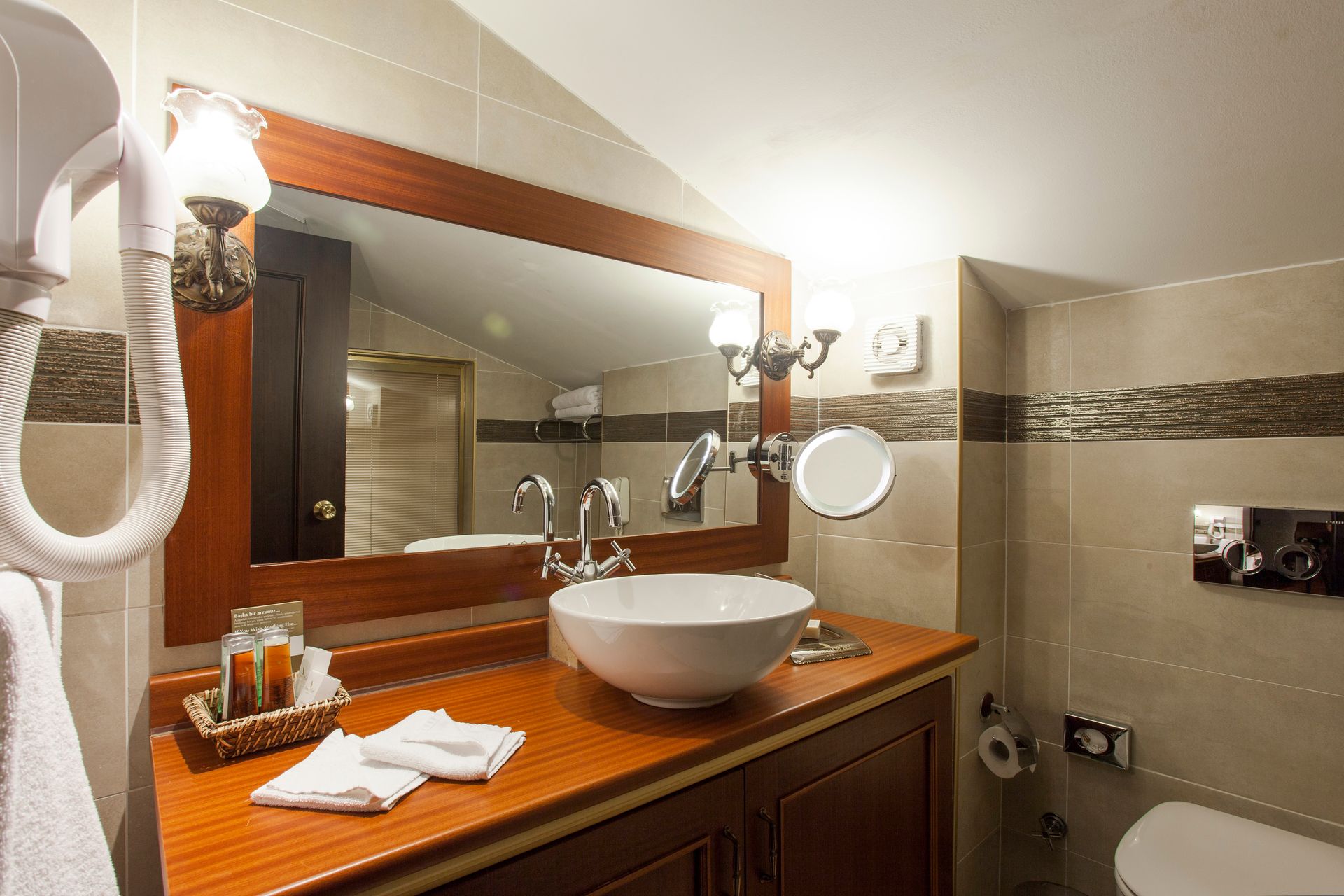 Bathroom with a wooden vanity, a white sink, large mirror, and a wall-mounted hairdryer.