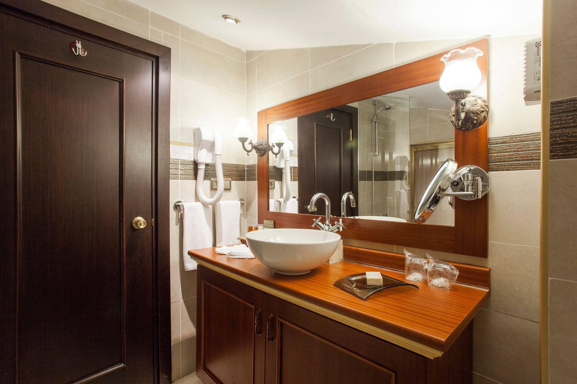 Bathroom with wooden vanity, white sink, large mirror, and dark brown door.