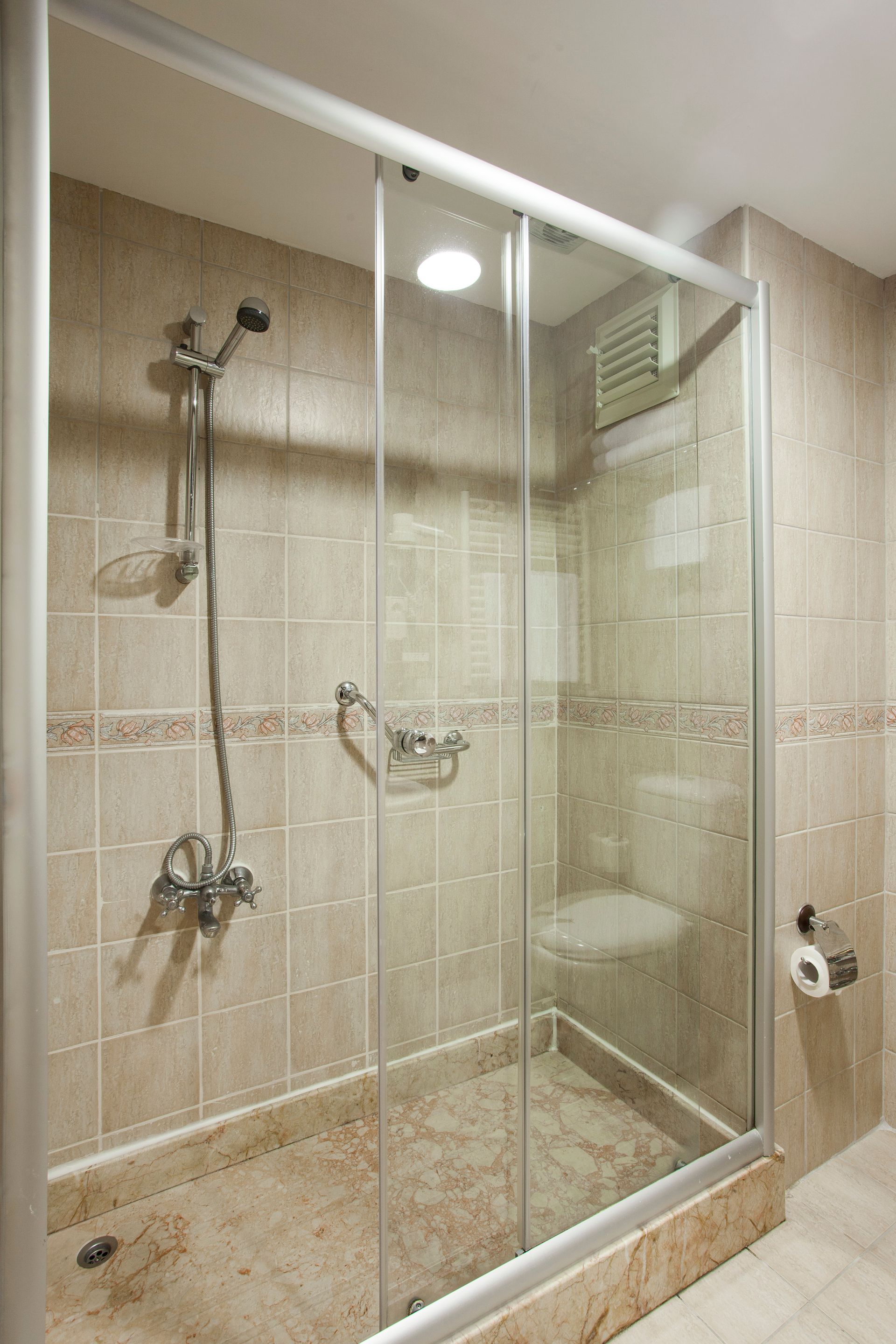 Shower stall with glass doors, silver frame, beige tile, and shower fixtures.