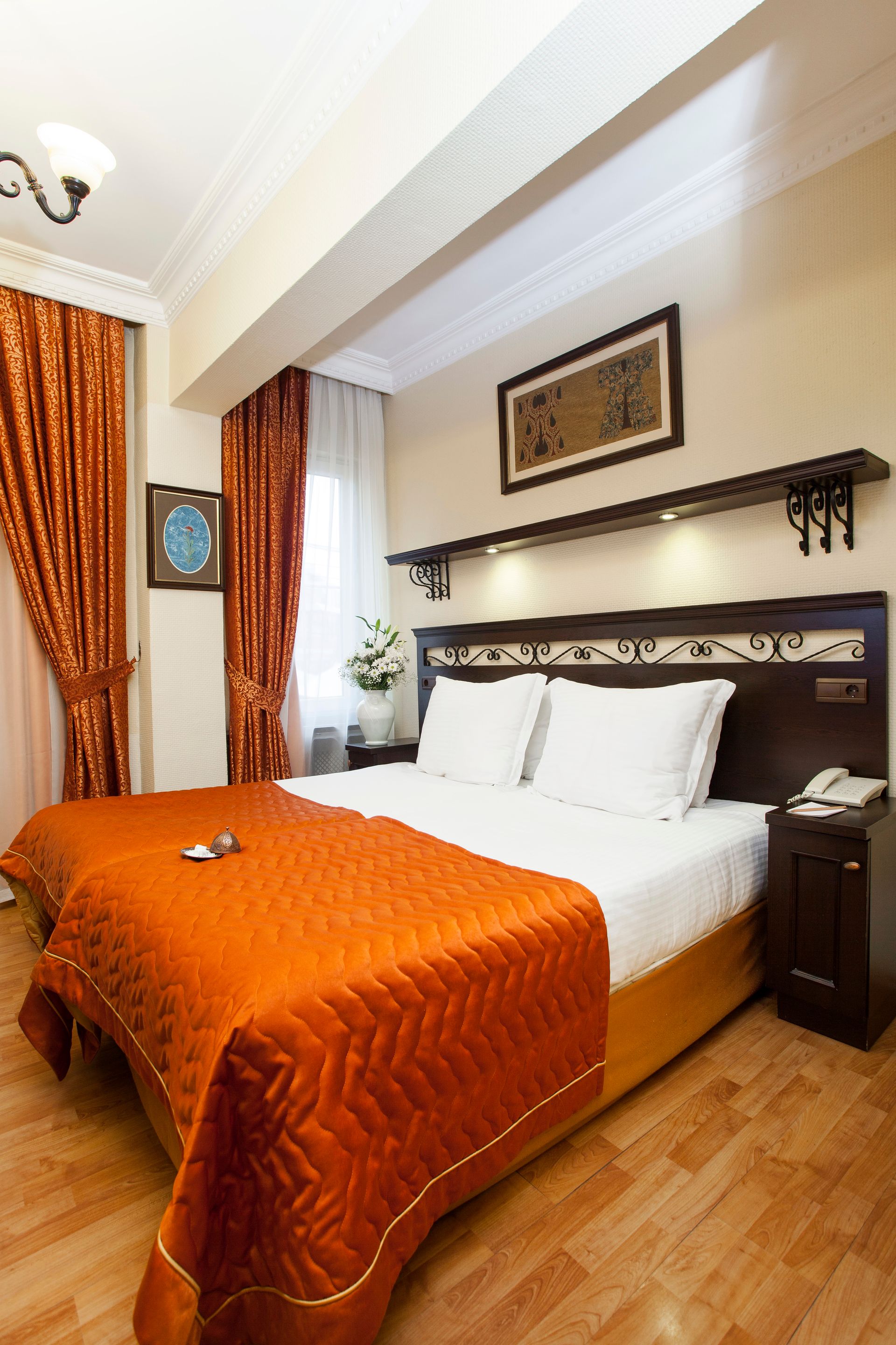 Hotel bedroom with a bed, orange bedding, wooden floor, and a framed art piece.