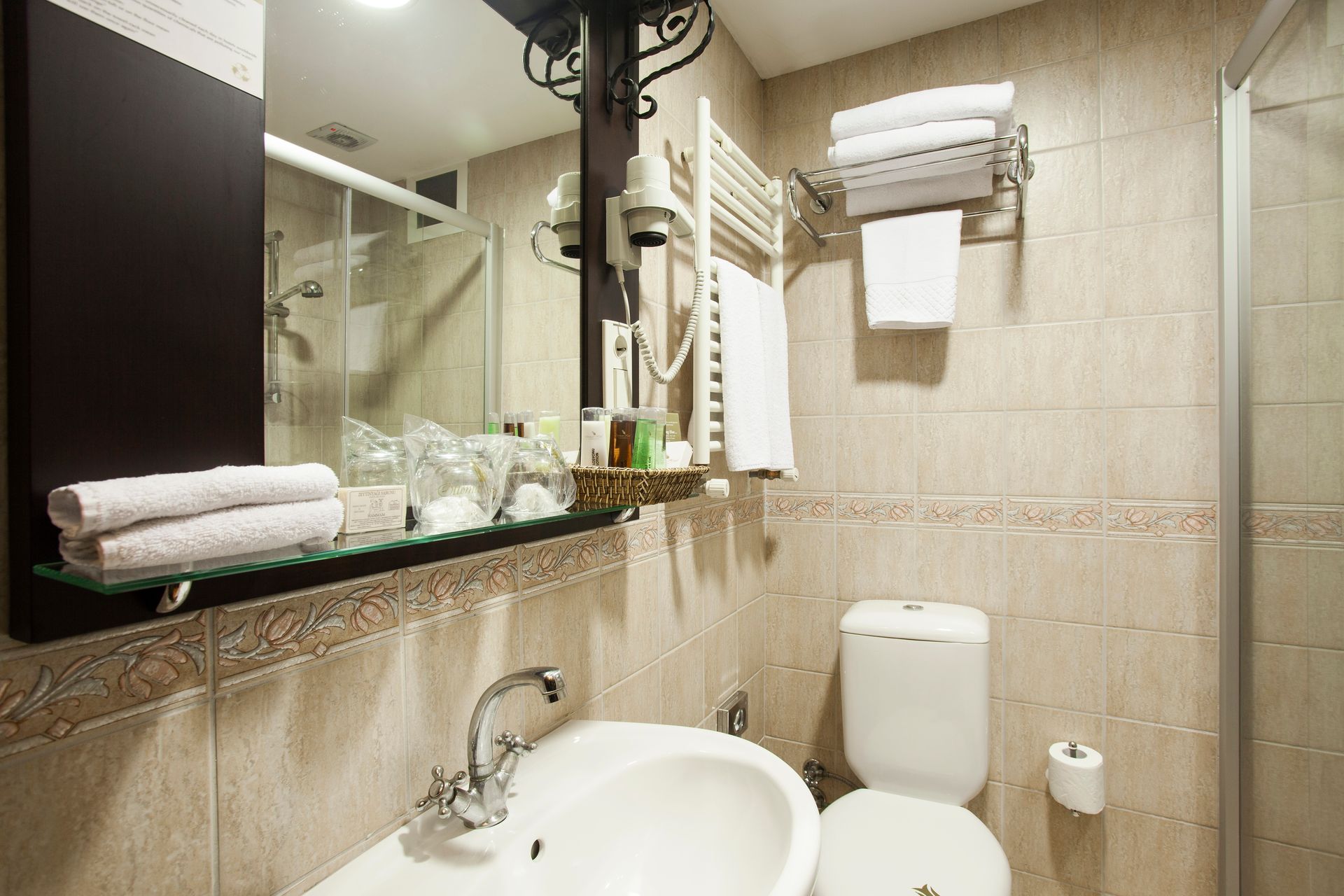 Bathroom with a sink, toilet, shower, and towels. Neutral tile and mirror.