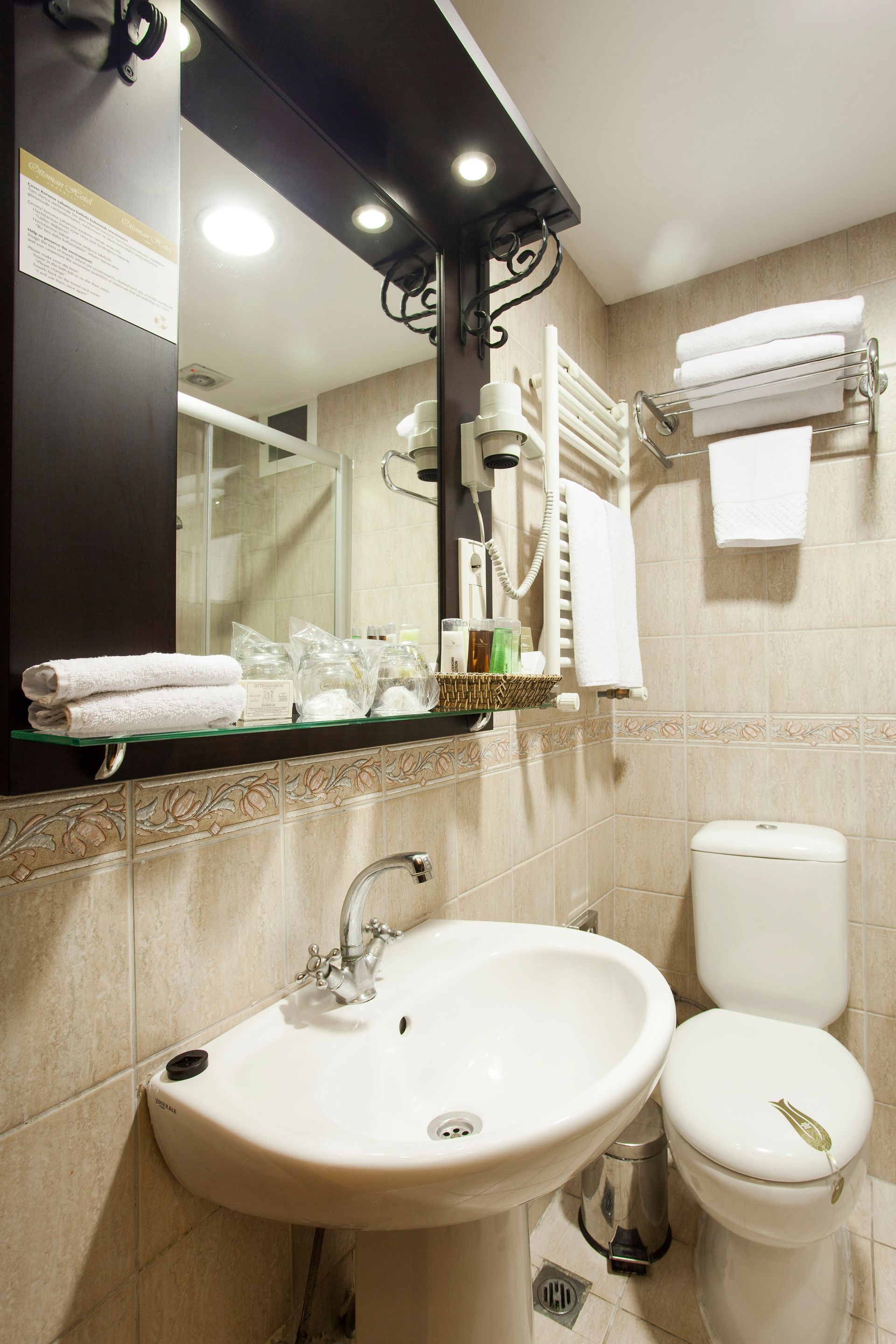 Bathroom with sink, toilet, mirror, and towels, beige tile walls.