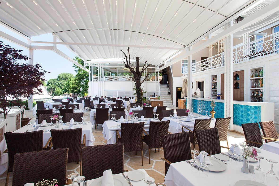 Restaurant patio with white tables, brown wicker chairs, and a retractable roof.