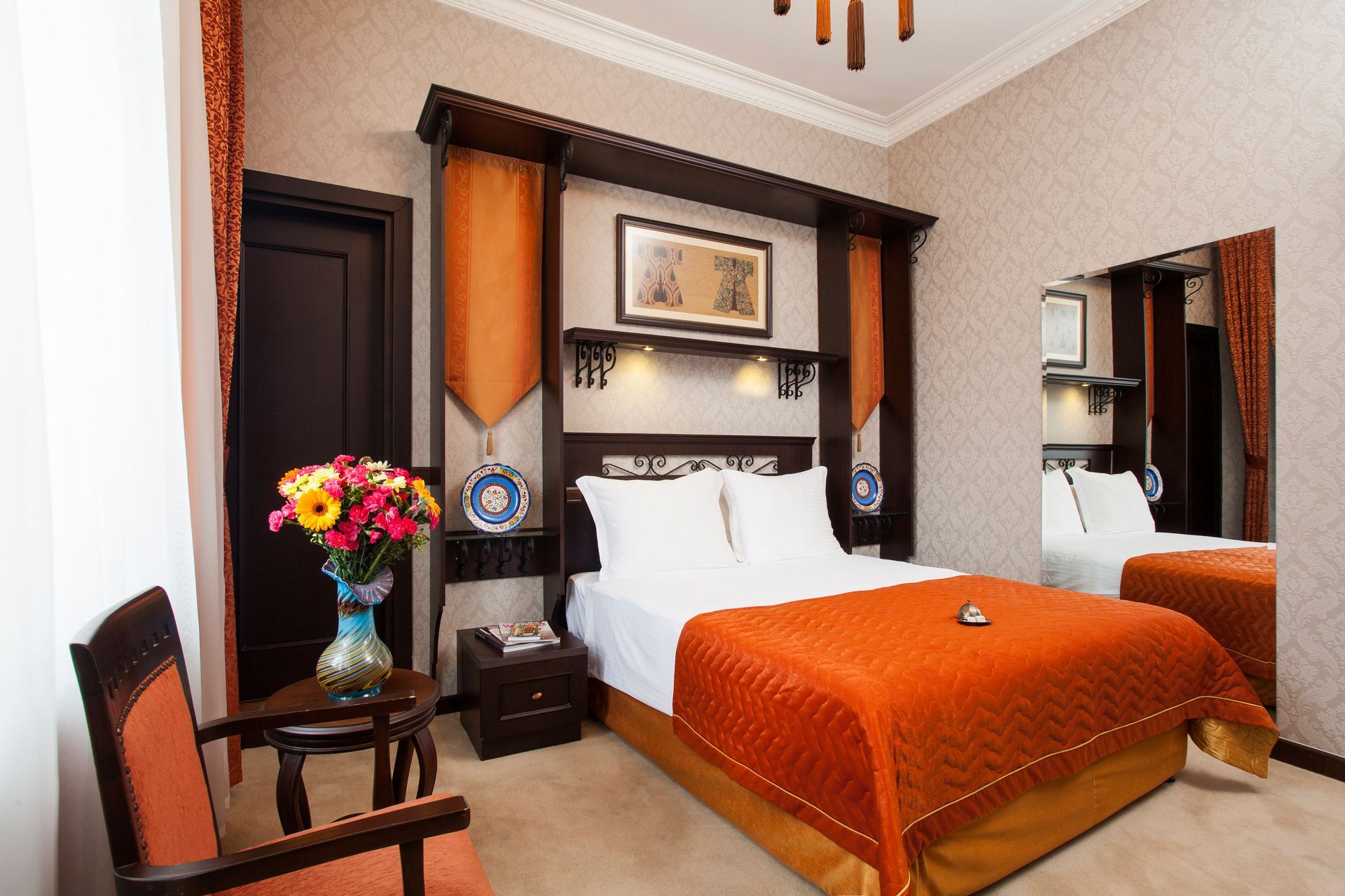 Ottoman Hotel, room with a queen bed featuring an orange quilted cover,  and a floral arrangement on a chair.