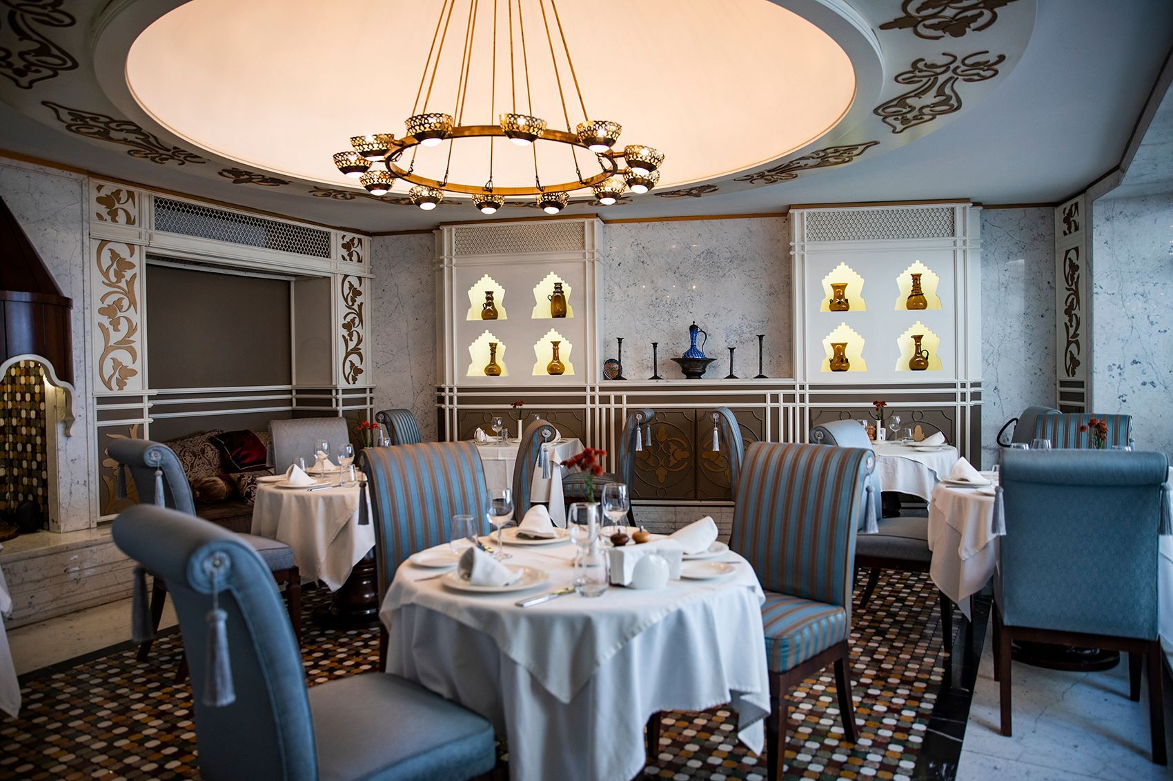 Elegant restaurant dining area with round tables, chairs, and ornate ceiling details.