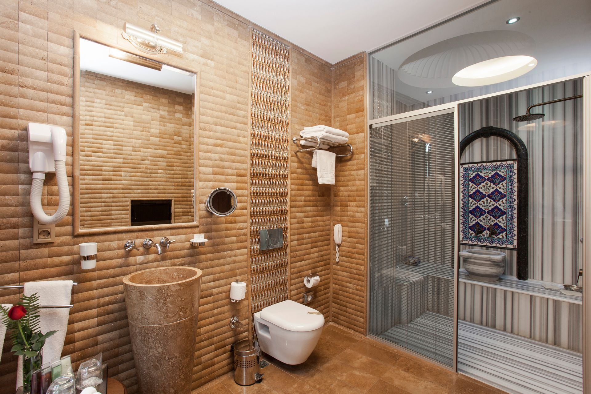 Ottoman Hotel, modern hotel bathroom with textured brown brick walls, a stone pedestal sink, , and a glass shower.