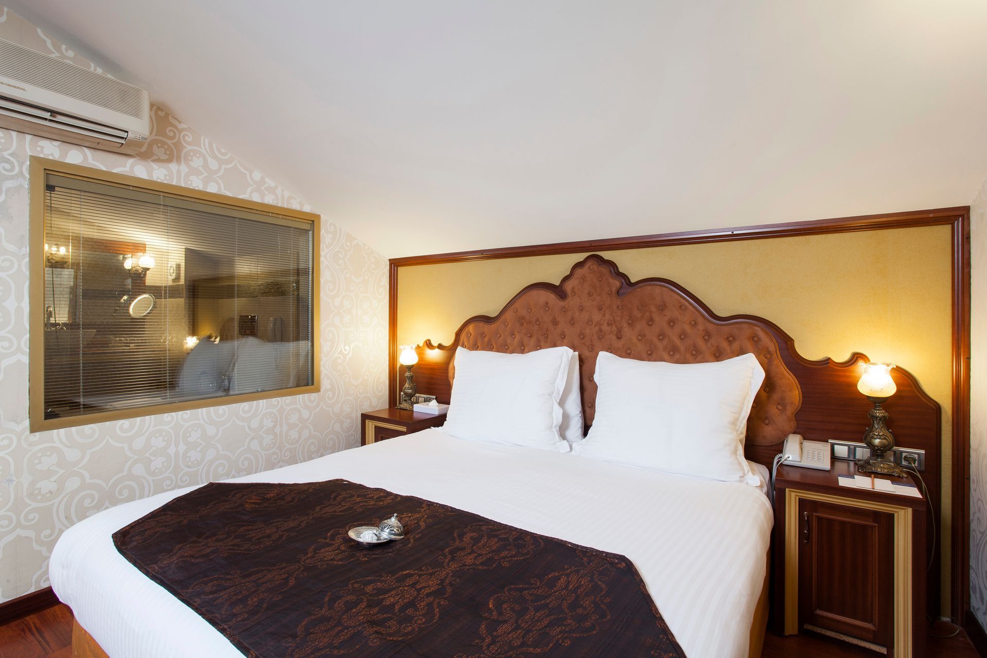 Bedroom with a large bed, decorative headboard, and a window with a view into a bathroom.