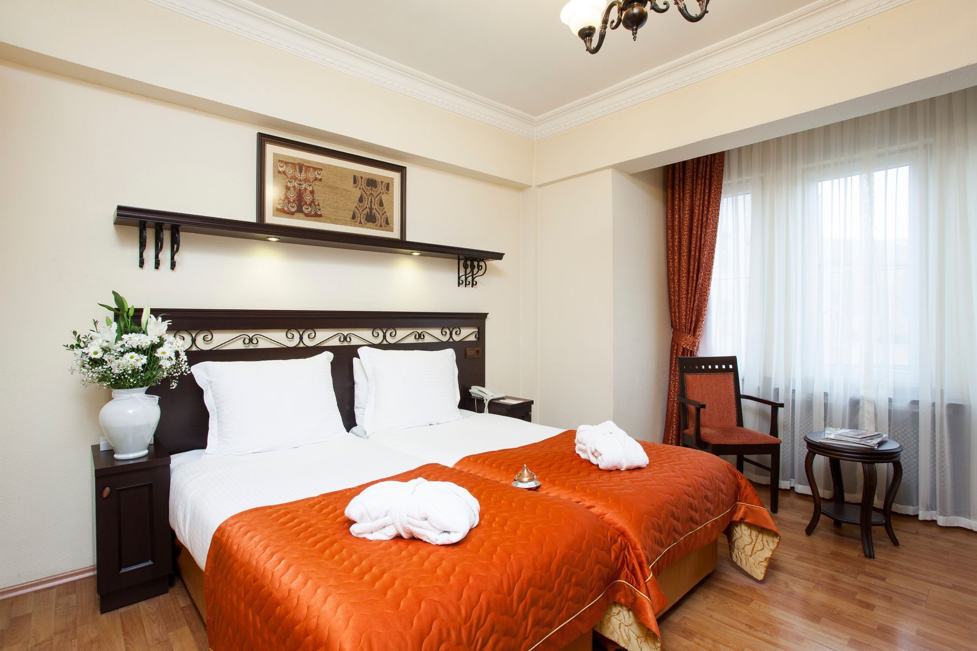 Hotel room with two beds, orange bedspreads, white linens, and a window with red curtains.