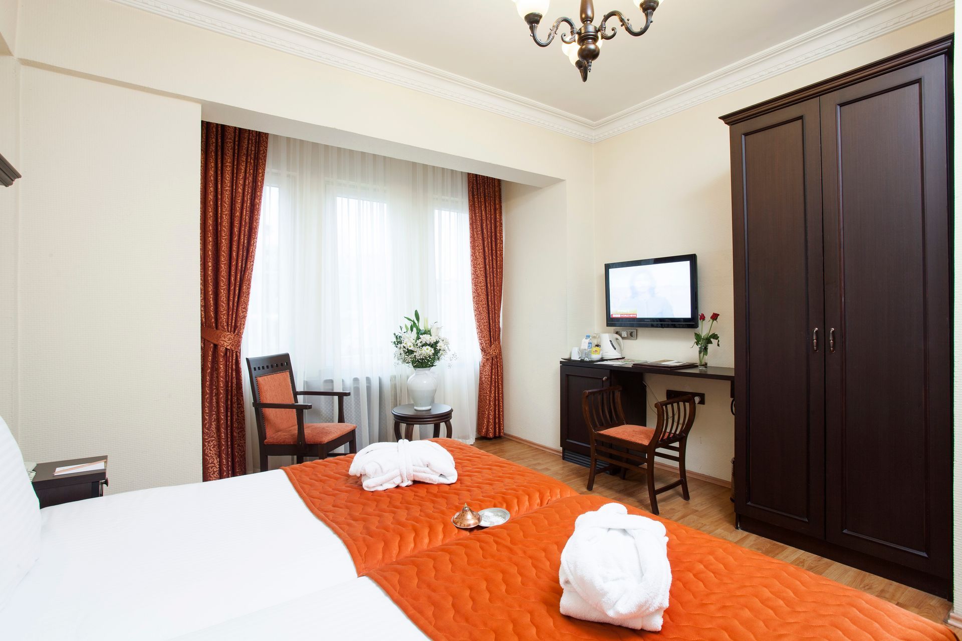 Hotel bedroom with a bed, TV, wardrobe, and window with curtains.