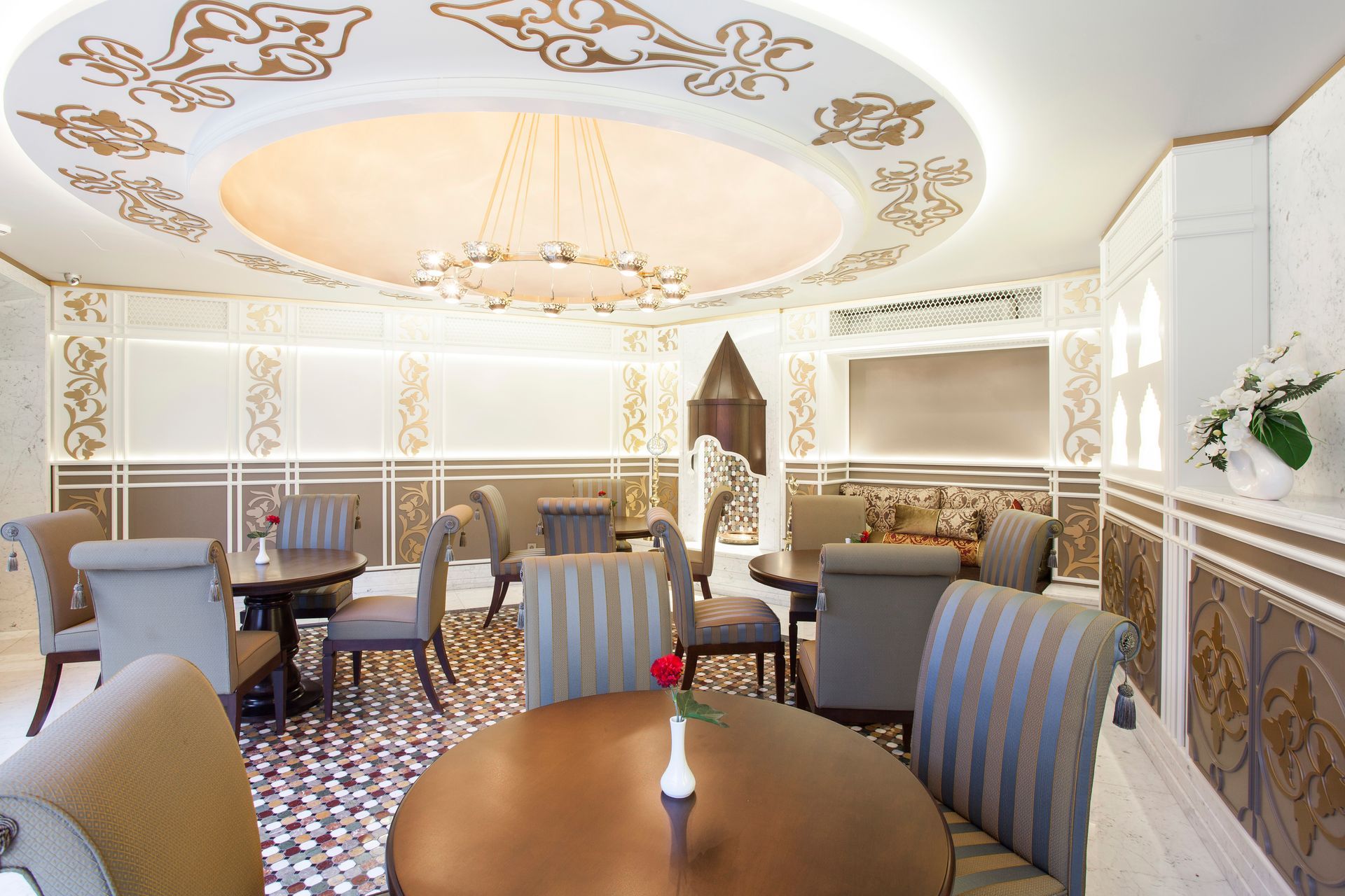 Elegant cafe interior with round tables and chairs, intricate ceiling designs, and decorative wall panels.
