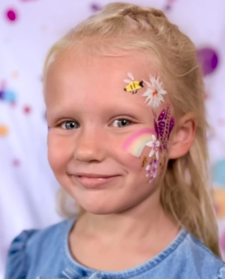 Blond meisje met gezichtsbeschildering: bij, bloem, vlinder en regenboog, lacht naar de camera.