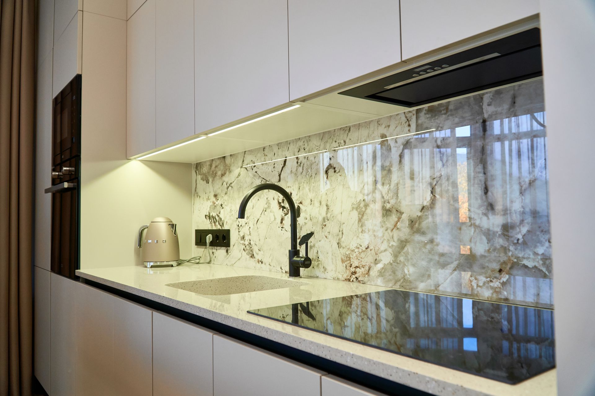 Modern kitchen with white cabinets, marble backsplash, black faucet, and built-in stovetop.