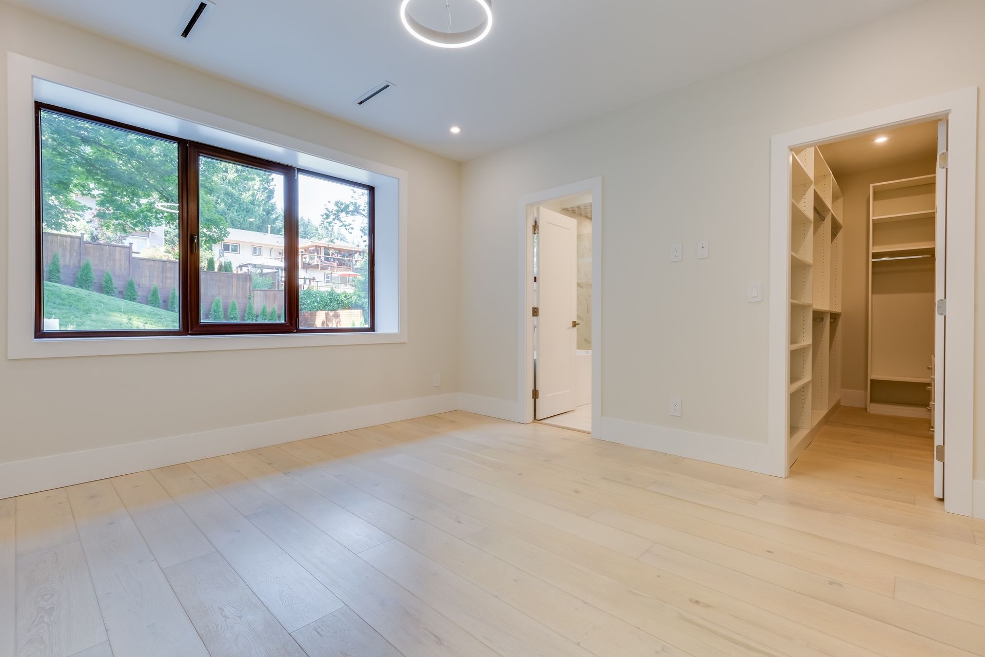 Bright empty room with light wood floors, large window, and open closet and doorway.