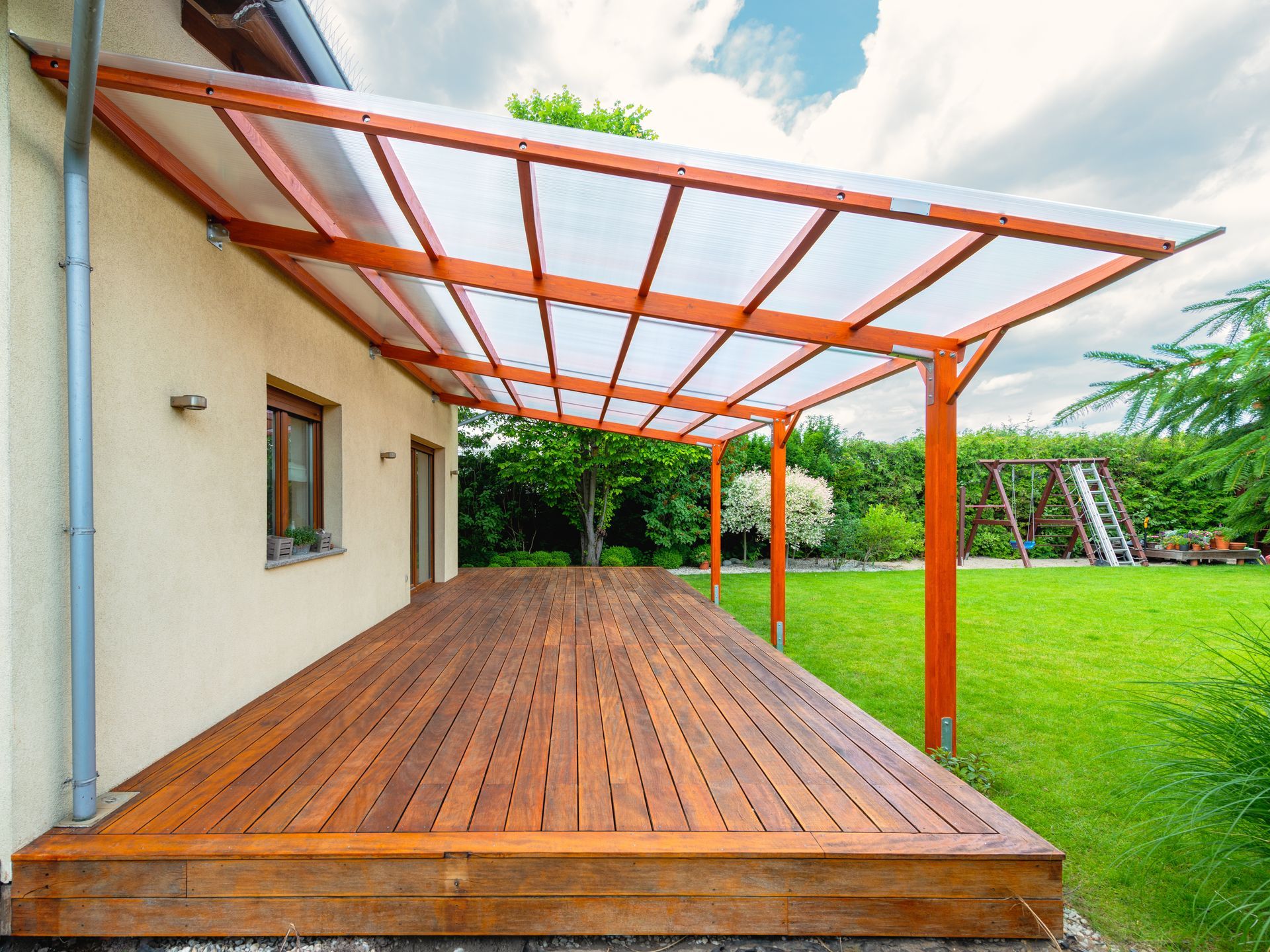 Wooden deck patio with a red pergola beside a house and green lawn