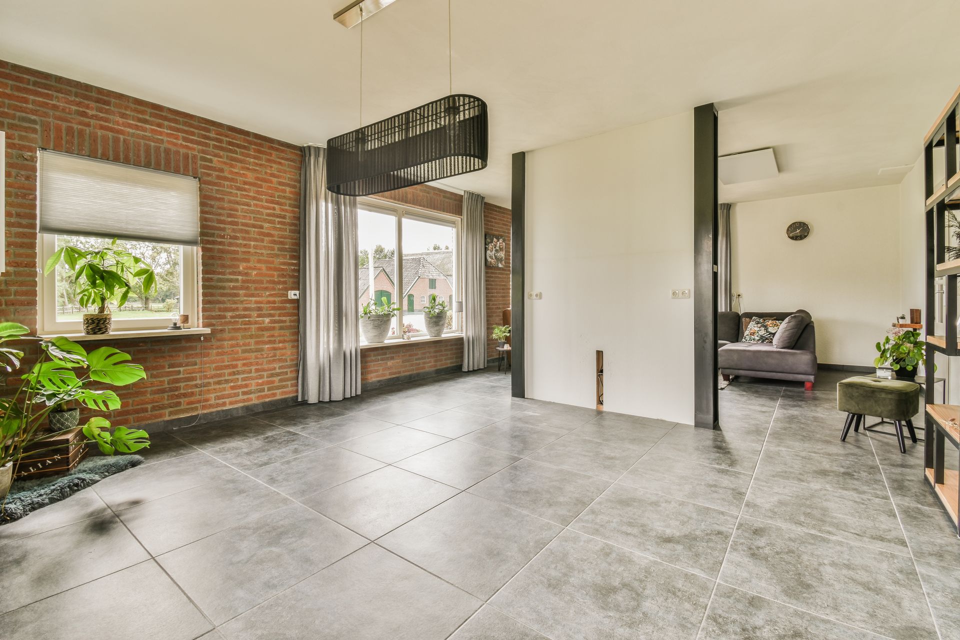 Spacious modern living room with exposed brick, large windows, gray tile floor, and a dark sofa nook