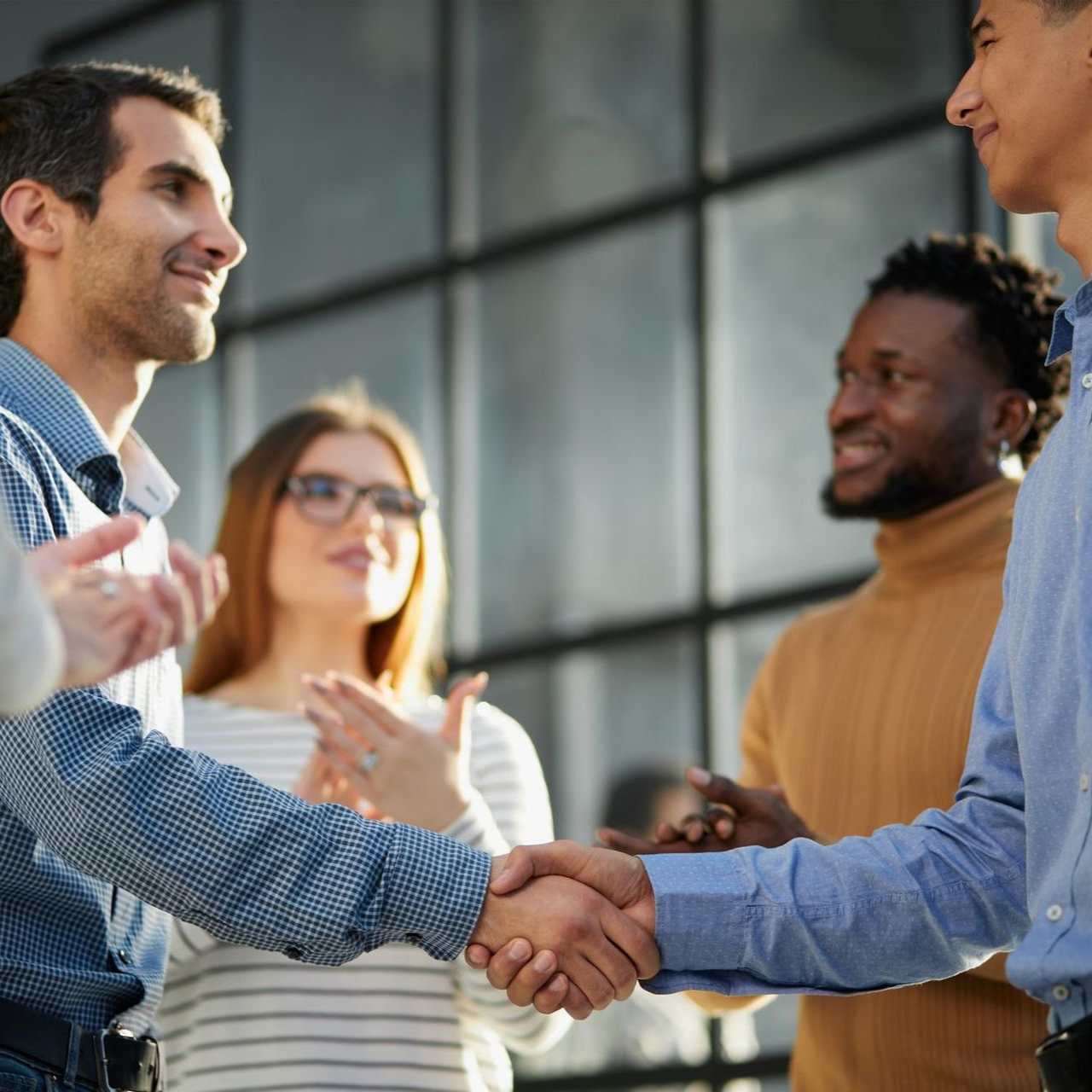 Two people shaking hands in an office with two colleagues smiling in the background