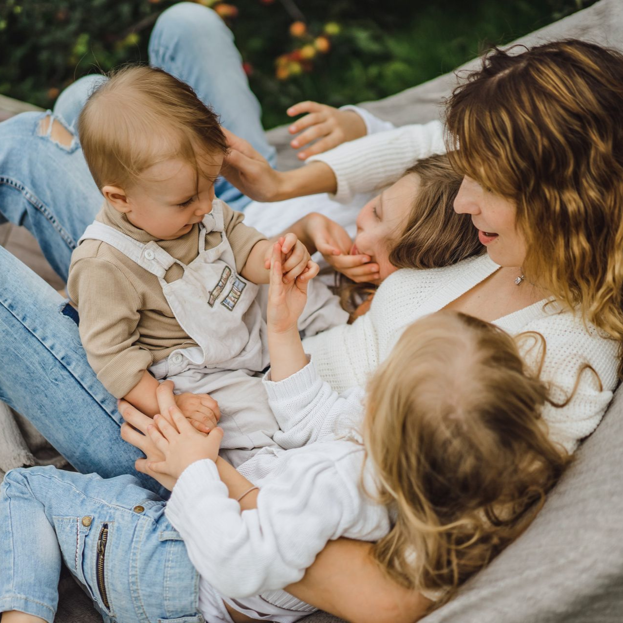 Family lounging on a blanket outdoors, two toddlers playing with an adult in a cozy garden scene