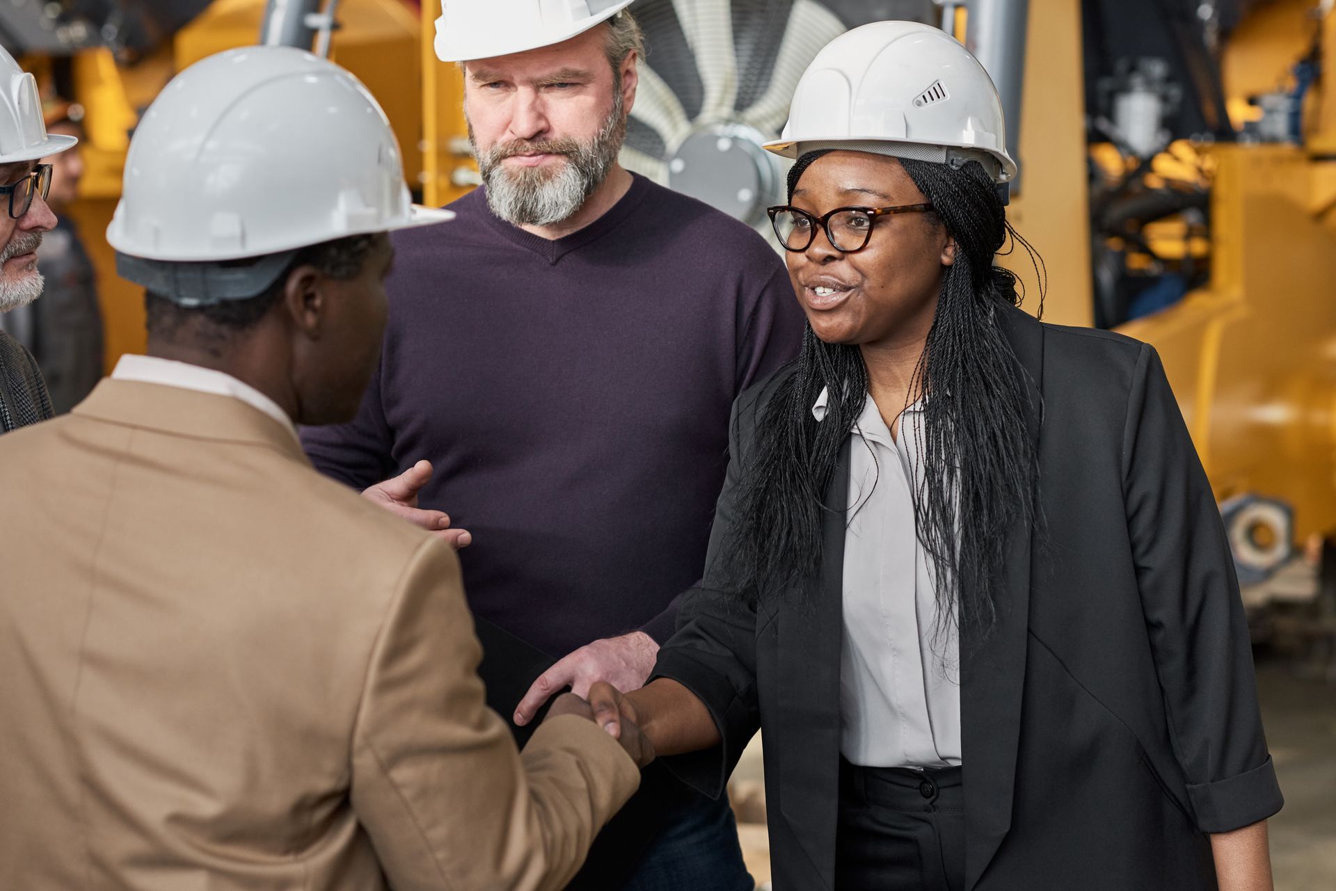 Three coworkers in hard hats shake hands at a factory site