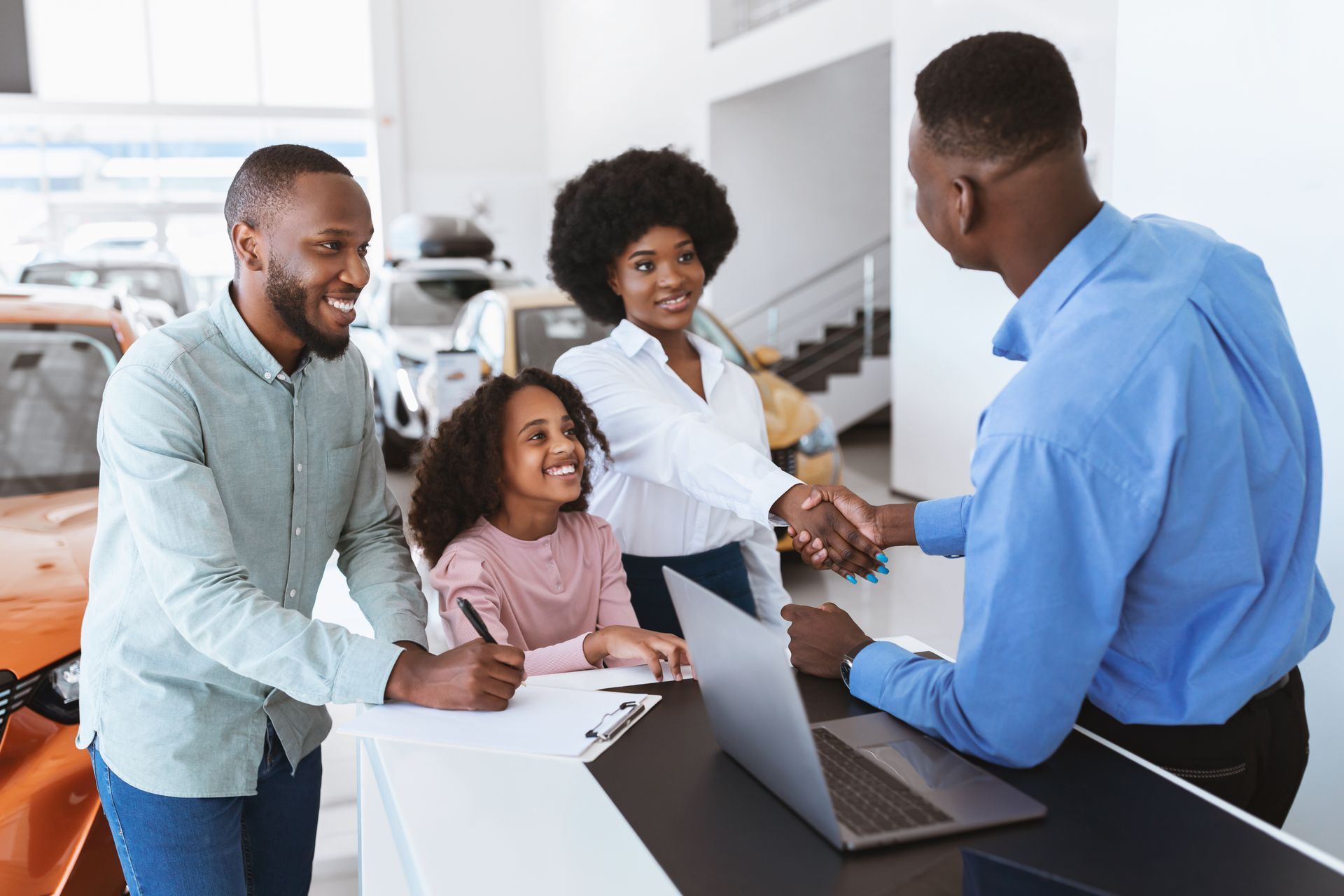Family talking with a sales agent at a desk in a bright office, with a laptop open.