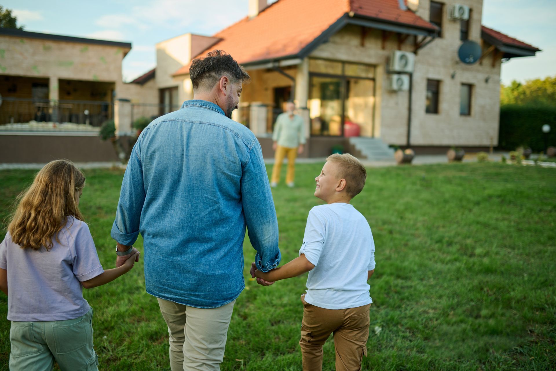Three people holding hands in a grassy yard outside a house at dusk