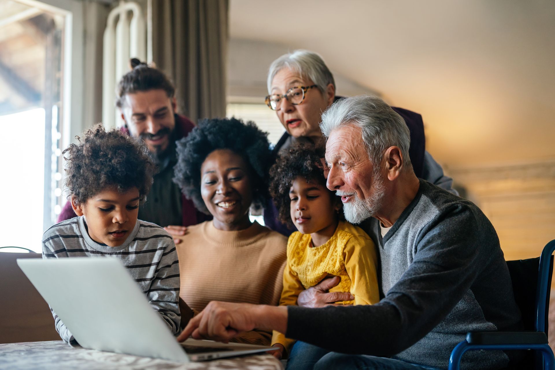 Family gathered around a laptop in a cozy living room, smiling and looking at the screen