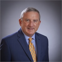 Professional headshot of a man in a blue suit and gold tie against a gray background
