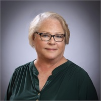 Portrait of a smiling person with glasses in a dark green blouse against a gray background