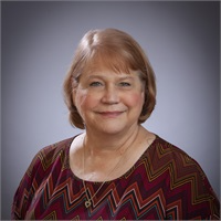 Smiling woman in a maroon patterned top against a gray studio backdrop