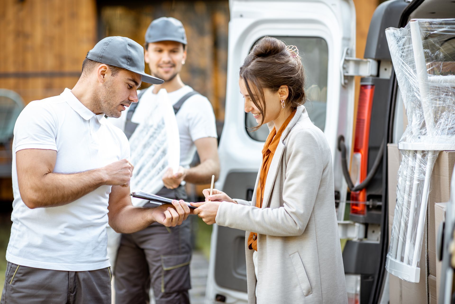 Two workers handing a clipboard to a woman beside a van with boxed equipment.