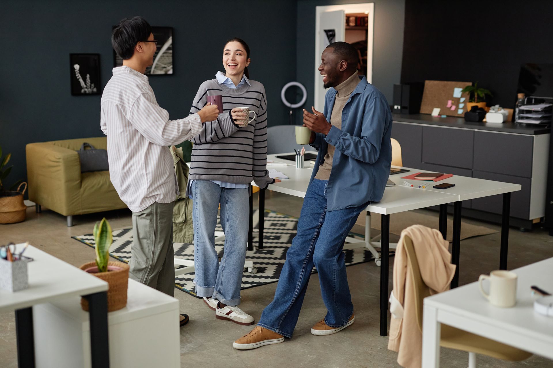 Three coworkers chatting and holding coffee mugs in a modern office lounge