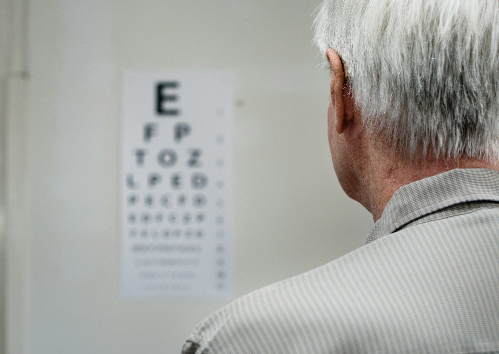 An individual faces an eye chart mounted on a wall during a vision examination.