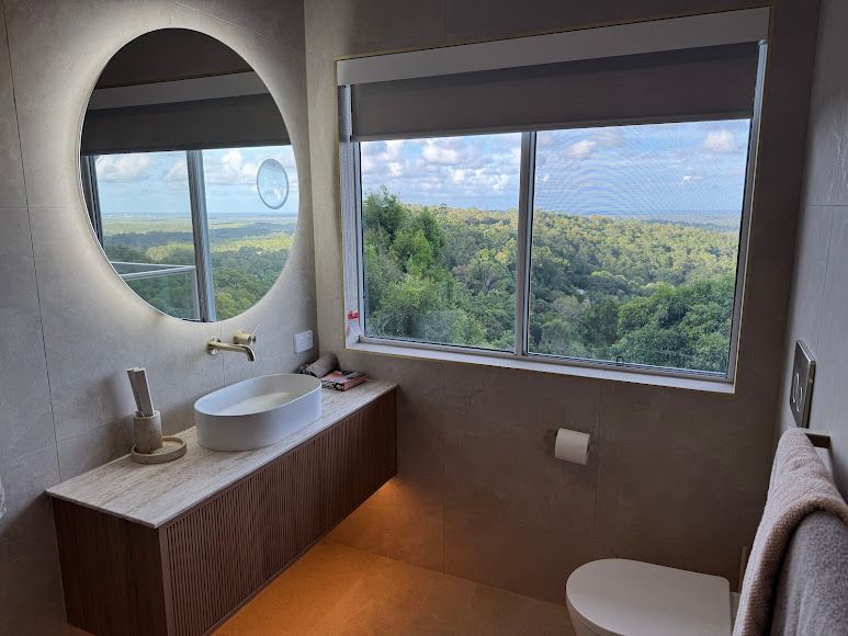 A Bathroom With a Toilet, Sink, Mirror and Window — Coastwide Plumbing Solutions in Mountain Creek, QLD