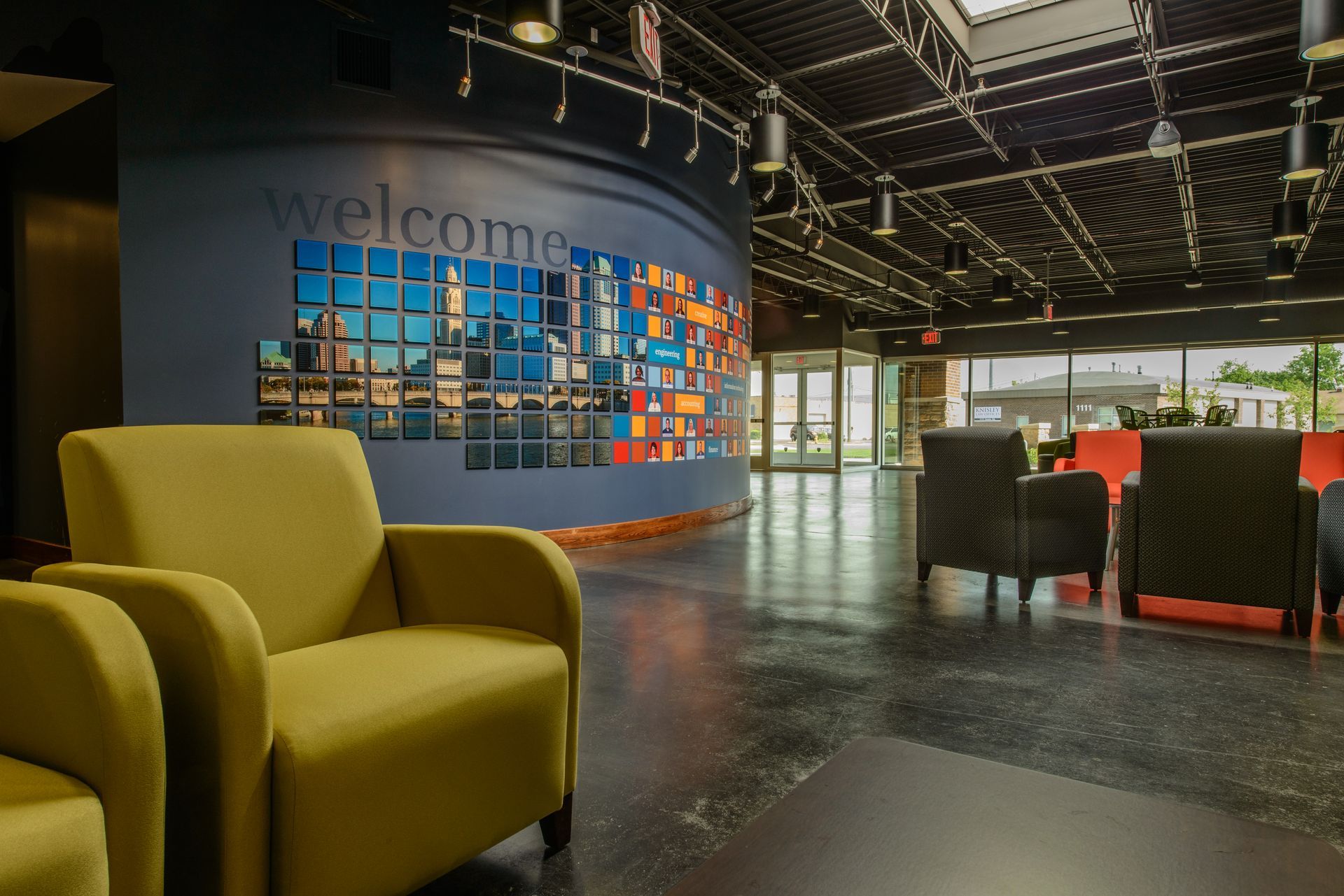 A modern waiting area with lime green chairs, a dark blue curved wall with a photo collage, and a dark tile floor.