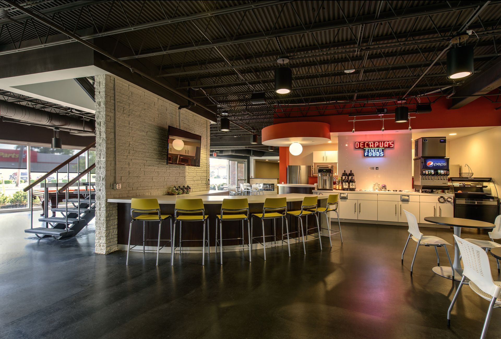 A modern office breakroom features a bar with yellow stools, pendant lighting, polished floors, and a fountain drink area.