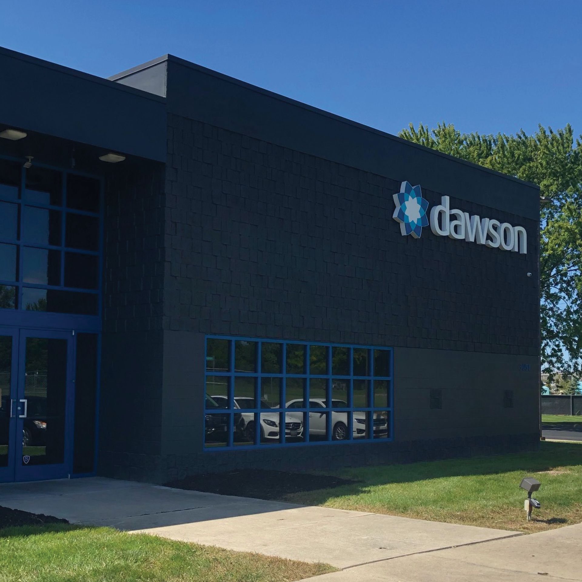 Dark blue building exterior with a Dawson company logo sign, glass windows, and a paved entrance under a clear blue sky.