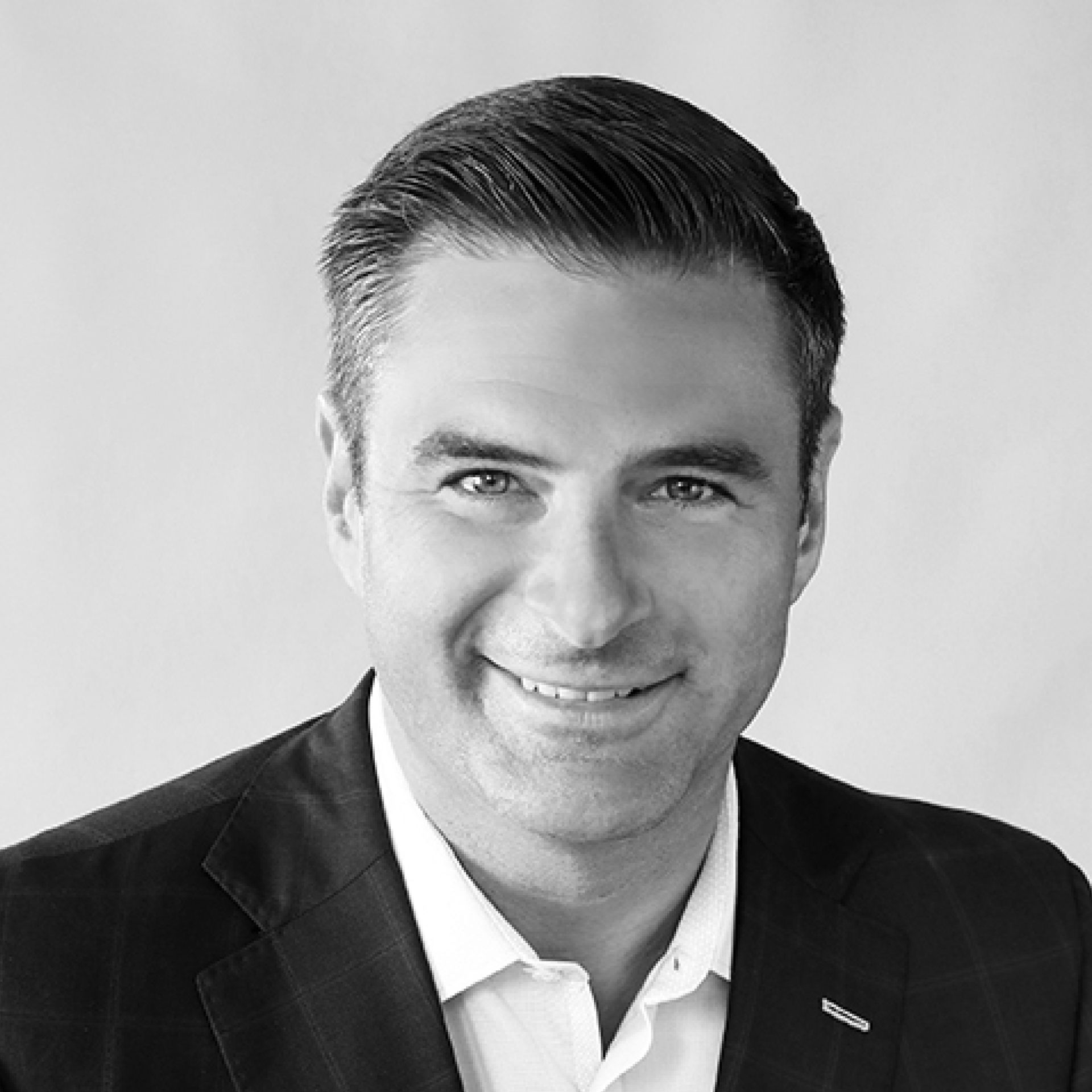 A black-and-white headshot of a smiling person wearing a collared shirt and blazer against a light, plain background.