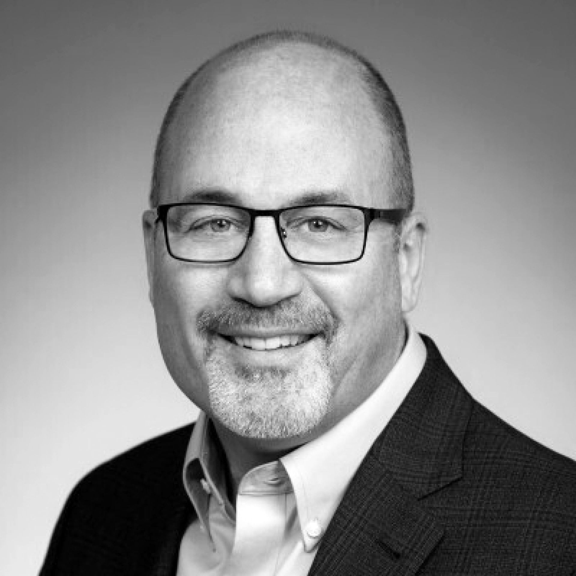 Headshot of a smiling man with glasses, a goatee, and a collared shirt under a blazer against a neutral background.