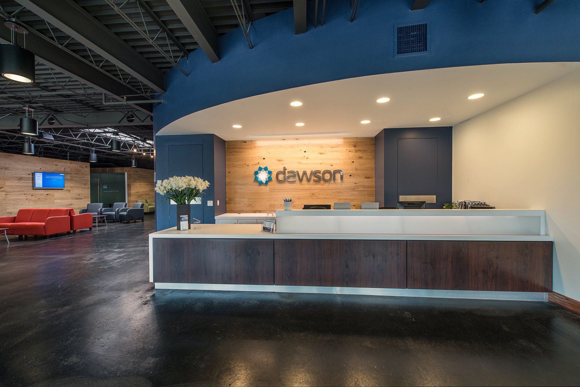 Modern office reception area featuring a long dark-wood desk, light wood-paneled wall with the