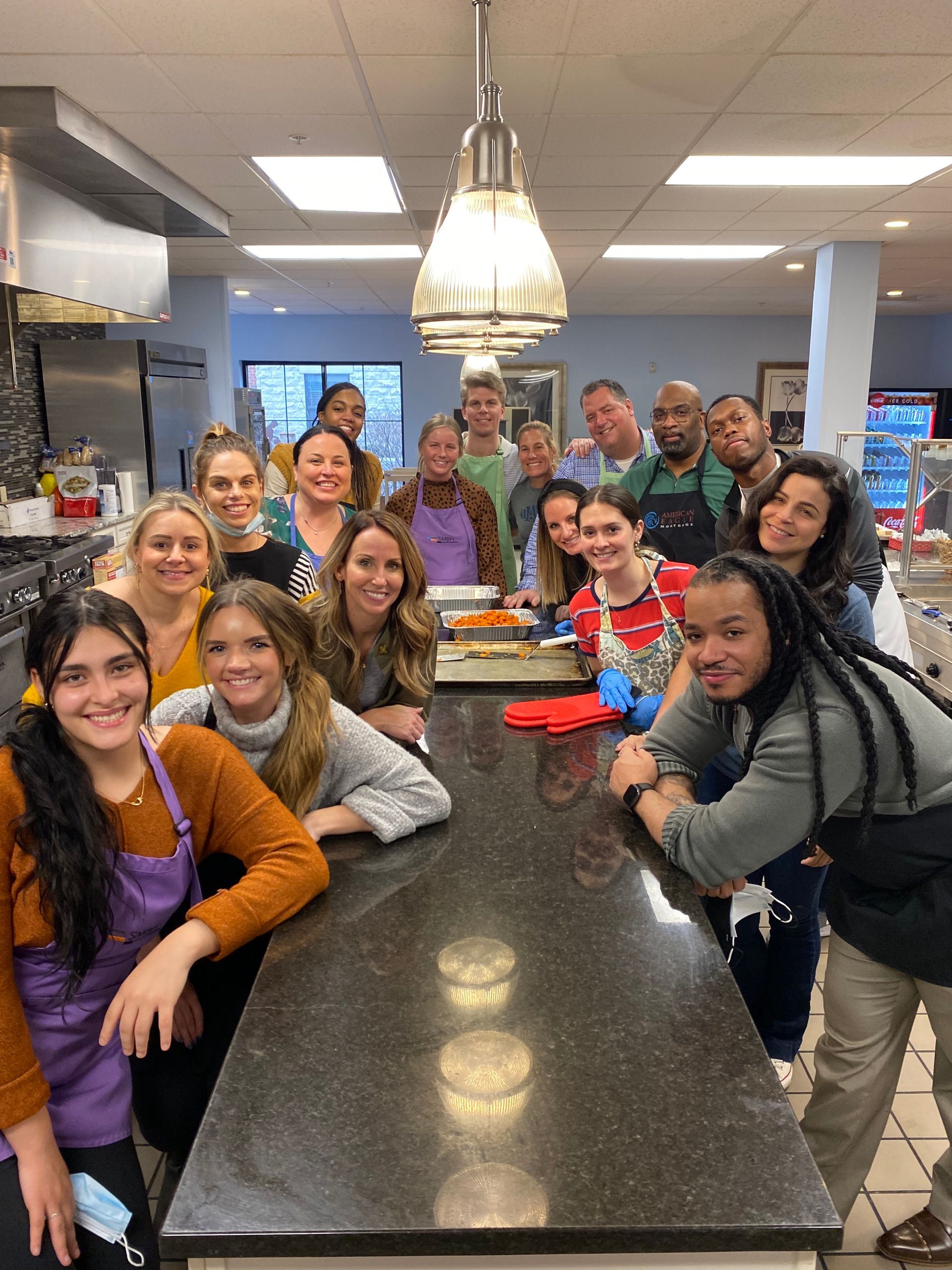 A diverse group of people posing for a photo behind a long kitchen island in a commercial kitchen setting.