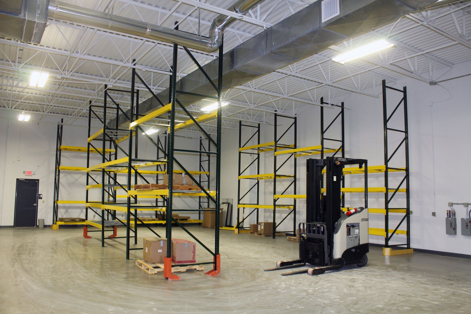 A warehouse interior features rows of empty black and yellow storage racks with a forklift parked in the center.